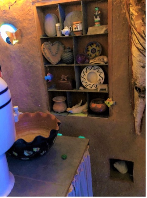 View of earth wall with shelf holding pottery and trinkets